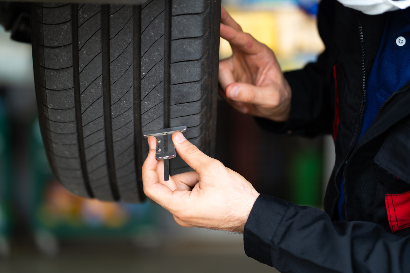 Mechanic checking checking the depth of car tire tread. Car maintenance and auto service garage concept.